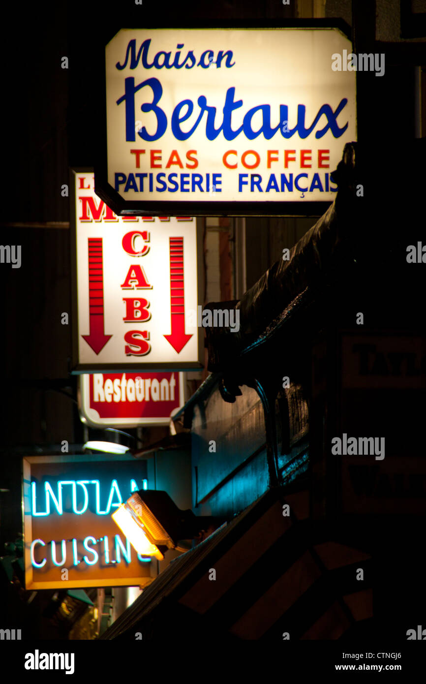 Signes sur rue grecque Soho sur la nuit Maison Bertaux patisserie, taxis, restaurant, la cuisine indienne, etc London England UK Banque D'Images