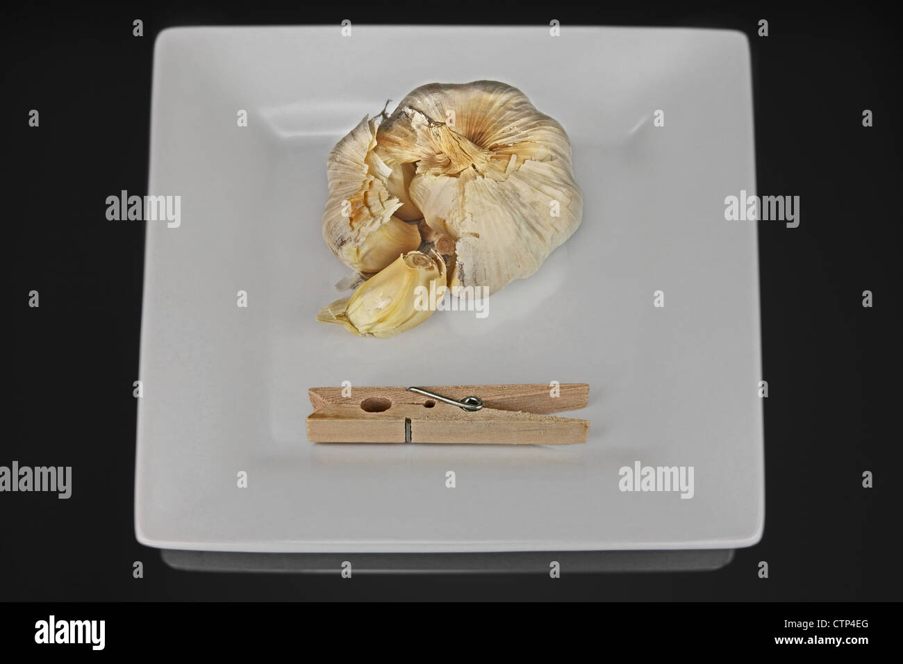 Un carré plat avec les gousses d'ail et un clothespin. La clothespin pince est de tenir votre nez. Tableau réfléchissant noir Banque D'Images