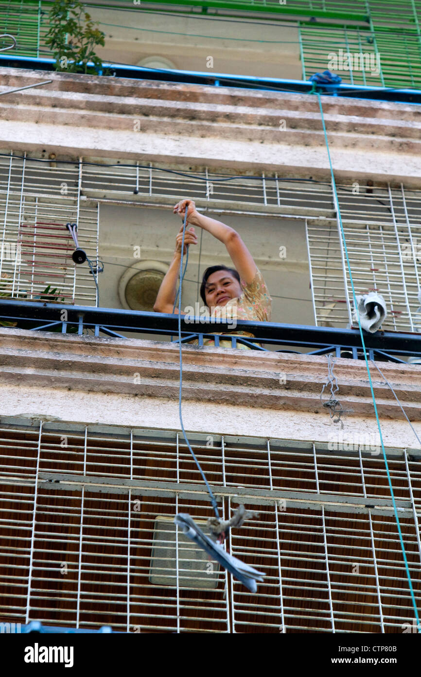Femme birmane de la réception d'une livraison d'un quotidien à l'étage supérieur d'un immeuble à appartements à Yangon (Rangoon), la Birmanie (Myanmar). Banque D'Images
