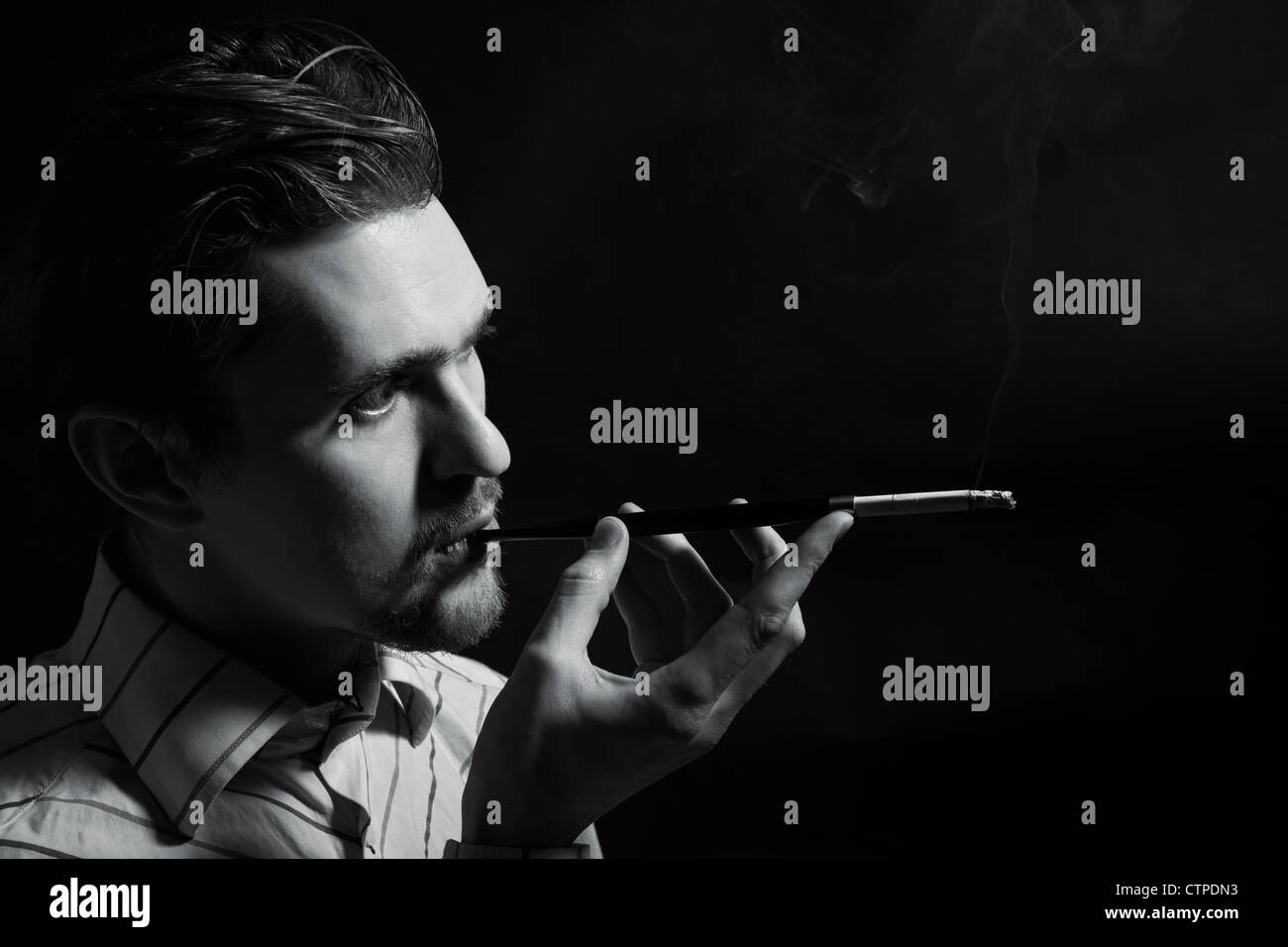 Studio Portrait of a young man smoking a cigarette sur fond noir Banque D'Images