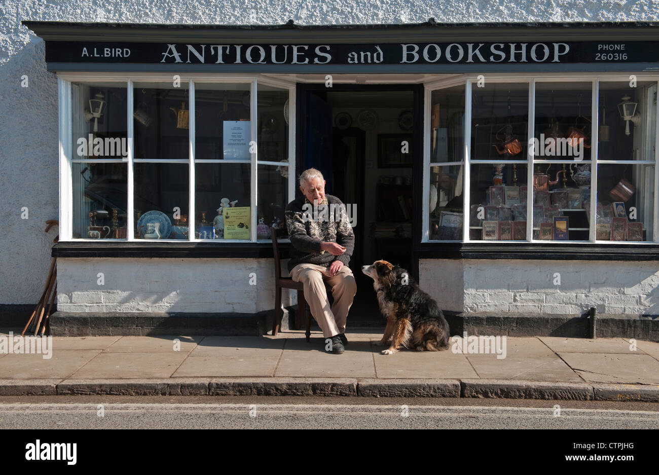 Le marchand d'antiquités Tony Bird est assis à l'extérieur de son magasin à Presteigne, Powys, Royaume-Uni, avec Sally le chien Banque D'Images