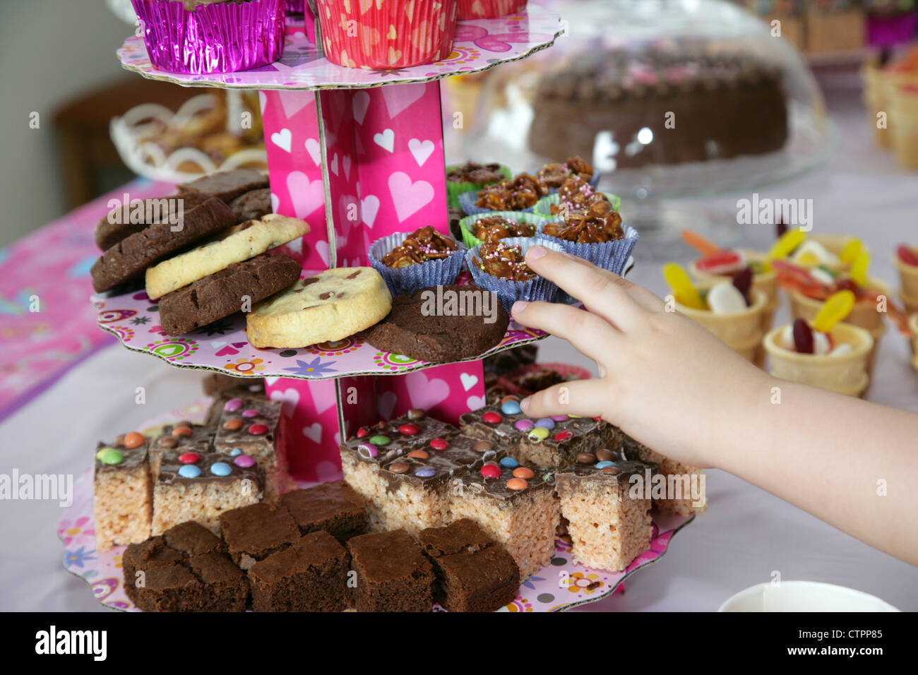 Childs hand reaching out pour aliments et boissons disposés sur une table pour une fête d'anniversaire des jeunes filles Banque D'Images