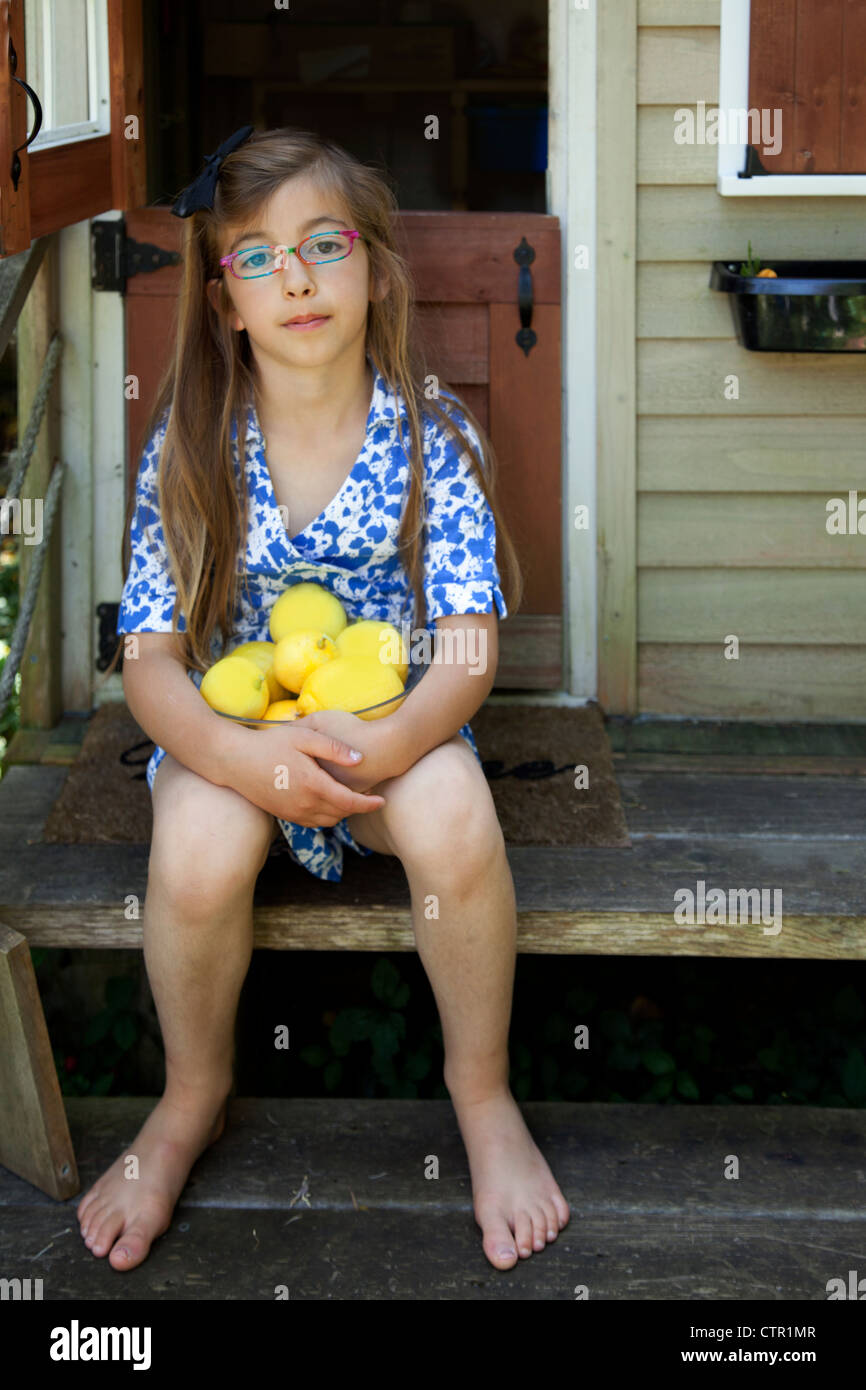 Une petite fille avec un bol de citrons est devant elle Playhouse. Banque D'Images