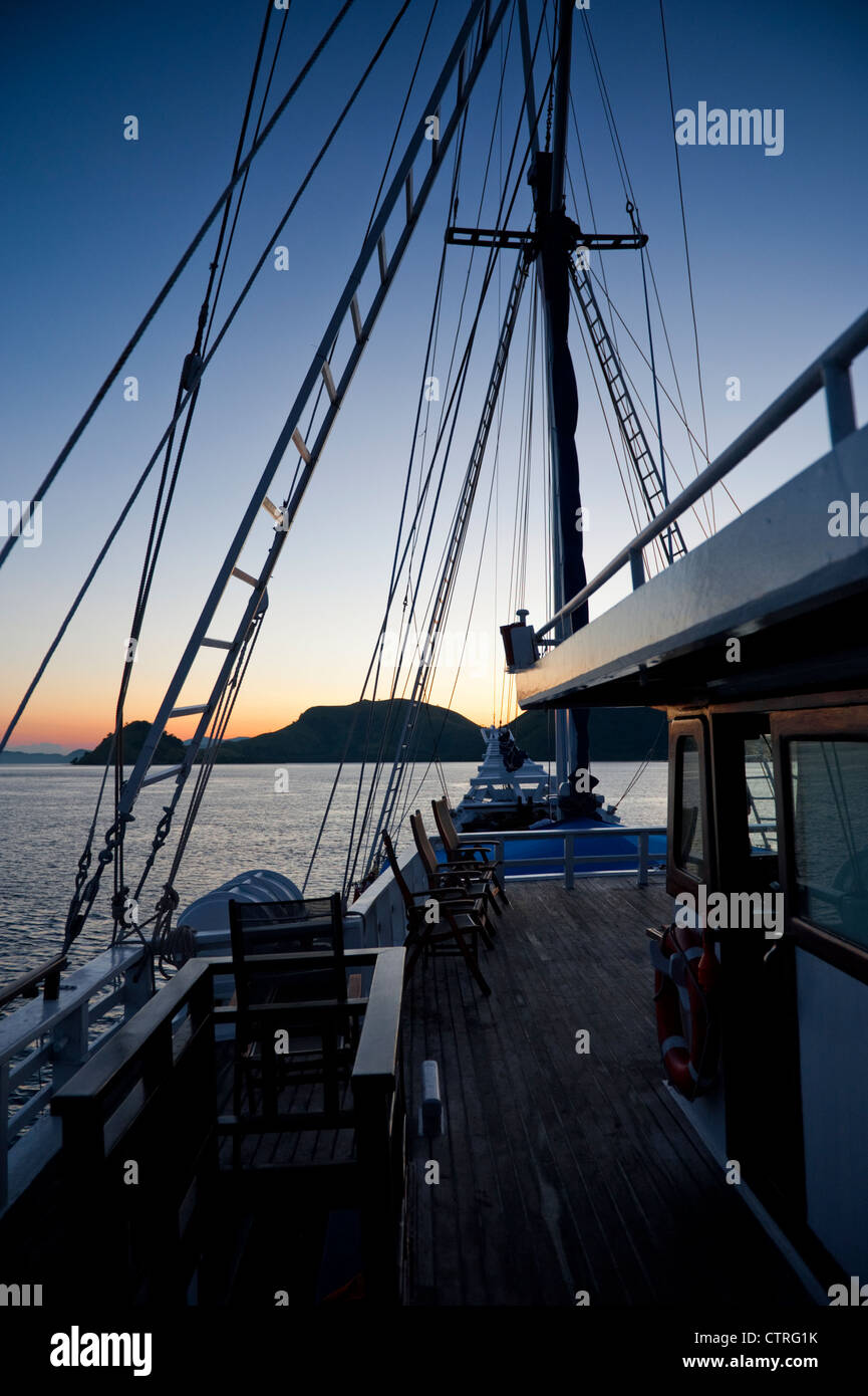 À bord du 'Ombak Putih' un Pinisi goélette traditionnelle en bois, l'île de Komodo est visible au lever du soleil dans l'arrière-plan. Banque D'Images