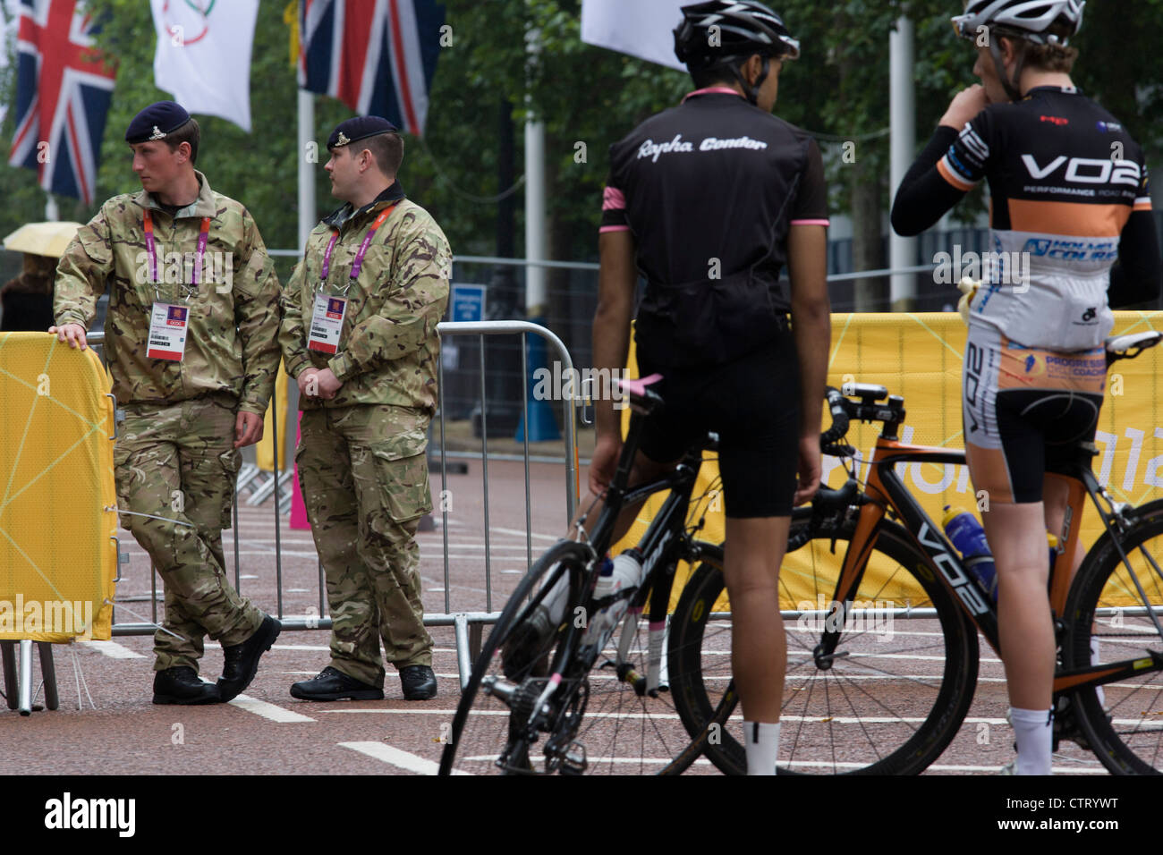 Les cyclistes avec les soldats du Royal Artillery Regiment de l'armée britannique se gardant l'entrée de la salle de volley-ball dans le centre de Londres à côté du logo sonneries du CIO au jour 4 des Jeux Olympiques de 2012 à Londres. 1 200 militaires sont déployés pour sécuriser les Jeux Olympiques de 2012 à Londres à la suite de l'échec par l'entrepreneur de sécurité G4S pour fournir assez de gardes privés. Le personnel supplémentaire a été rédigé dans l'malgré la persistance des craintes que la sécurité privée de la manipulation de l'entrepreneur €284m Durée du contrat demeure un risque pour les Jeux. Banque D'Images