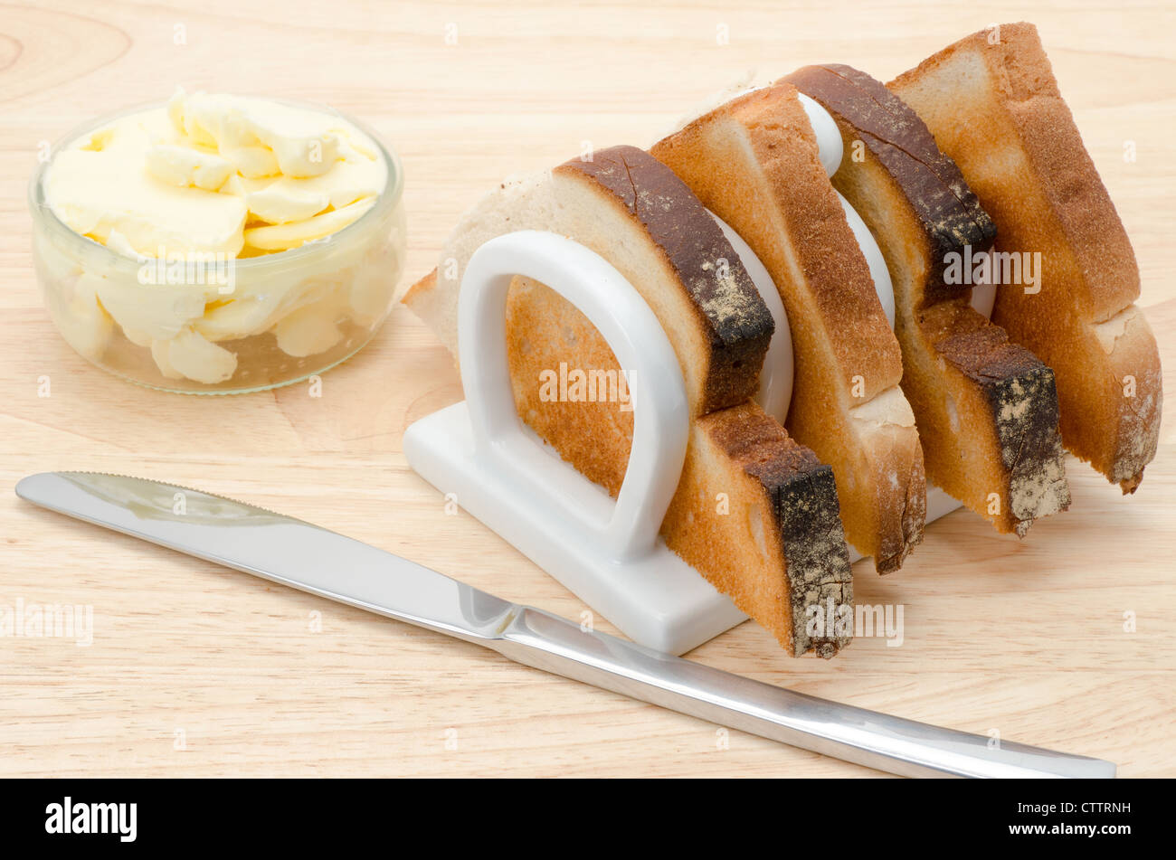 Tranches de pain grillé dans un rack blanc chine toast avec du beurre et un couteau de table. Banque D'Images