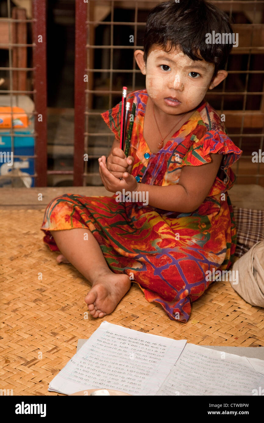 Le Myanmar, Birmanie. Petite fille birmane, crayons, Bloc-notes et de l'écriture. Elle a thanaka coller sur son visage, un cosmétique crème solaire. Banque D'Images