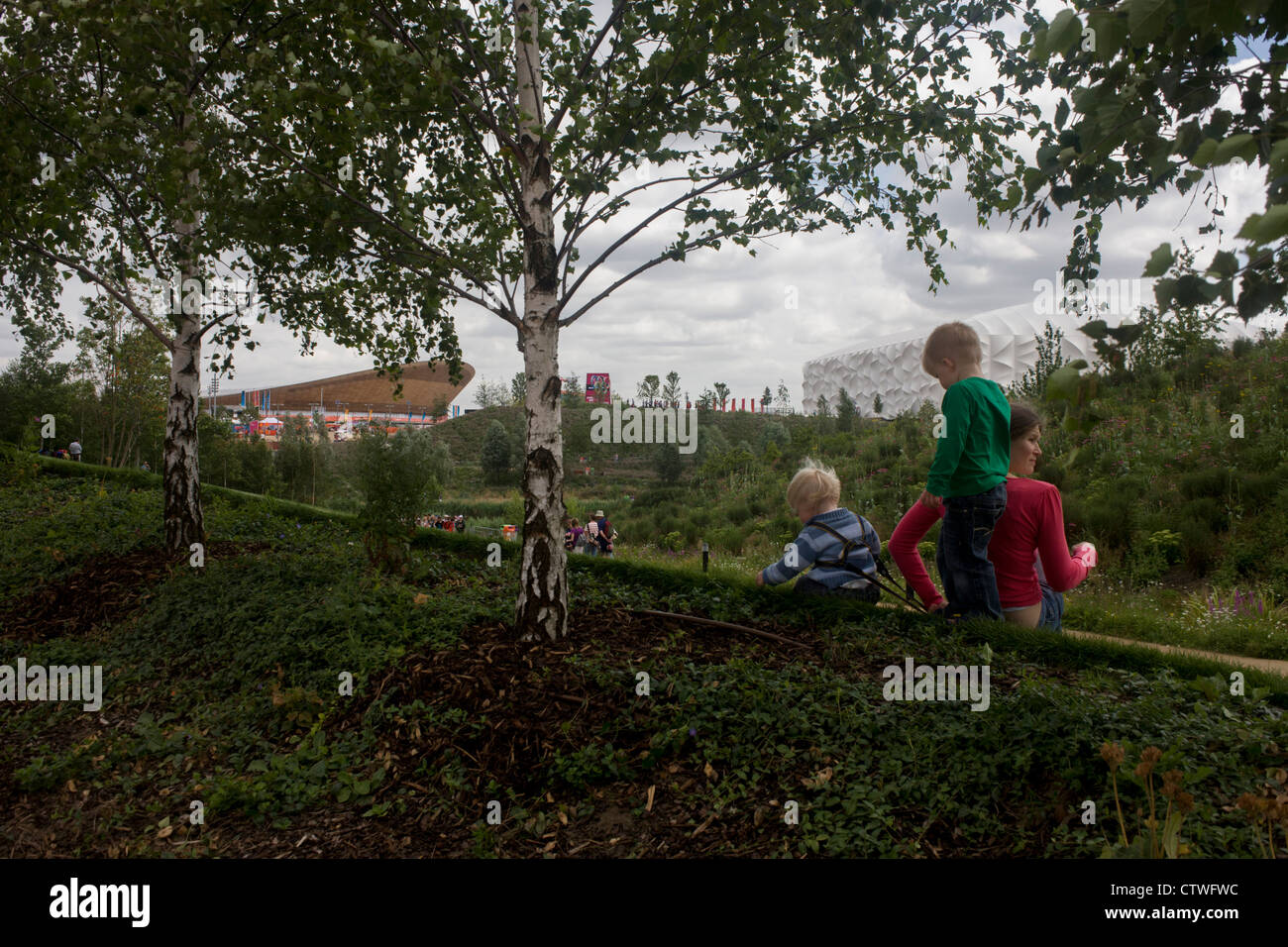 Les jeunes spectateurs d'admirer les fleurs de jardin anglais avec le stade olympique principal et de basket-ball arena dans l'arrière-plan pendant l'Jeux olympiques de 2012 à Londres. Le Parc olympique de Londres, à moins d'un kilomètre carré, est le plus grand nouveau parc dans la ville depuis plus de 100 ans. La plantation de 4 000 arbres, 300 000 plantes de milieux humides et plus de 150 000 plantes vivaces plus riches en nectar de fleurs sauvages faire un cadre coloré pour les Jeux. Banque D'Images