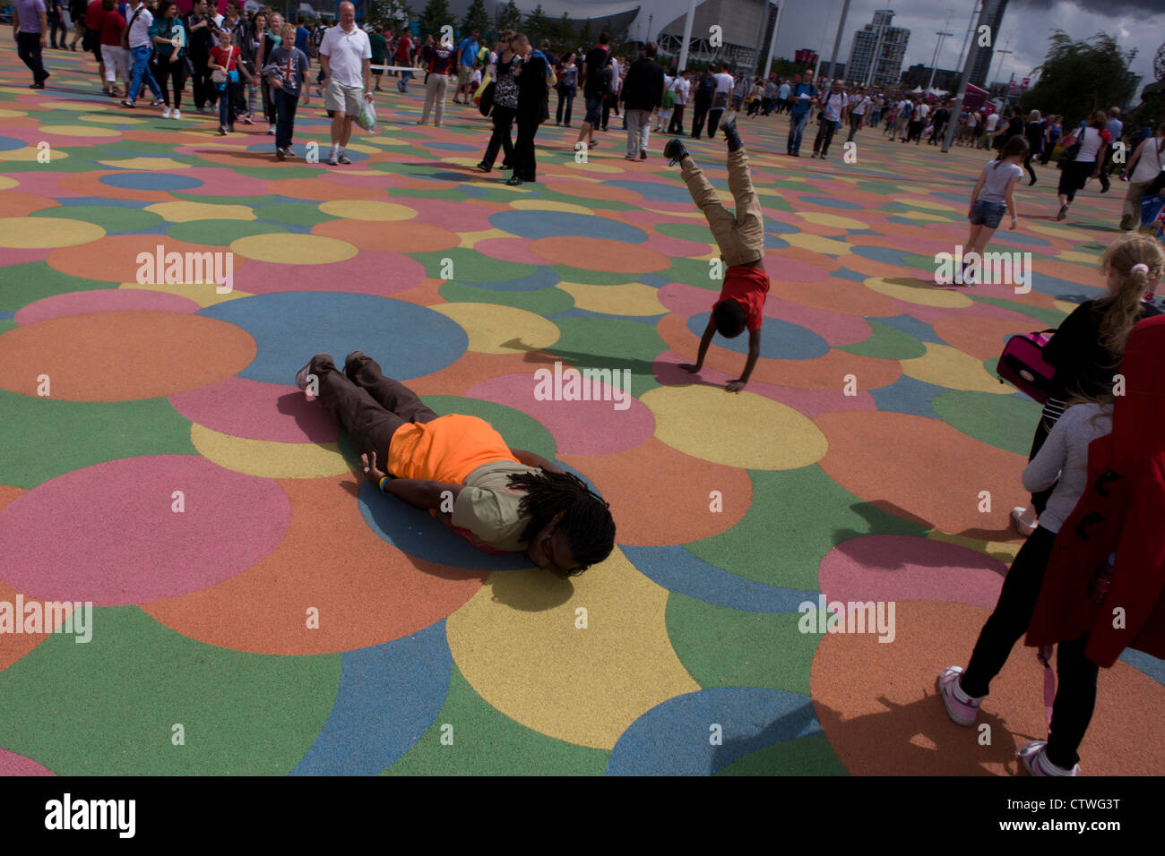 Spectateurs profitez de l'étage à motifs en forme de grille dans le Parc olympique au cours de l'Jeux olympiques de 2012 à Londres. Comme un enfant a une roue, une française se trouve sur le terrain de poser pour une photo de famille. Ce terrain a été transformé pour devenir un 2,5 Km2 complexe sportif, une fois que les entreprises industrielles et maintenant le lieu de huit salles dont l'arène principale, centre aquatique et le vélodrome et le Village Olympique des athlètes. Après les Jeux Olympiques, le parc est d'être connu sous le nom de Queen Elizabeth Olympic Park. Banque D'Images