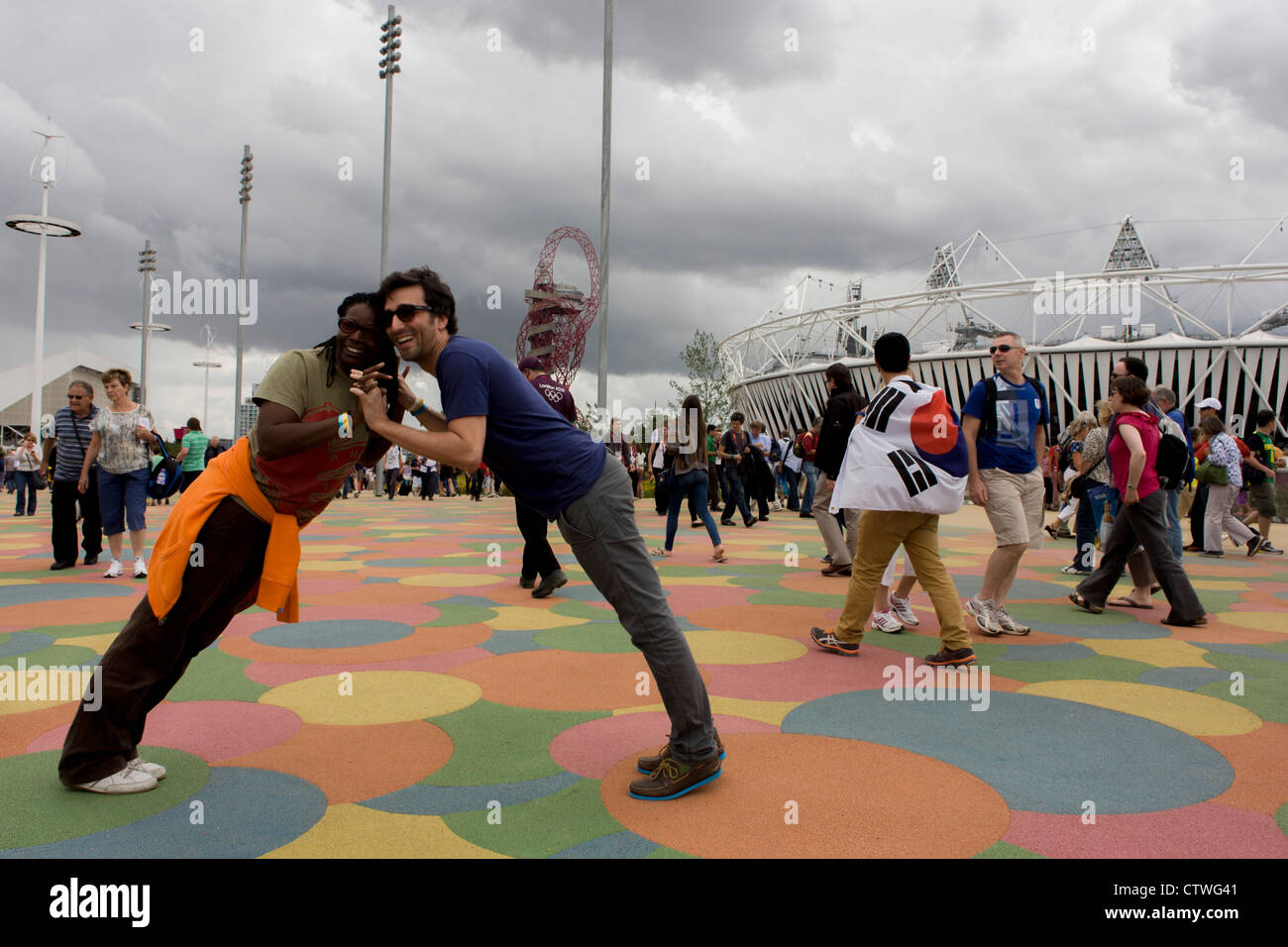 Spectateurs profitez de l'étage à motifs en forme de grille dans le Parc olympique au cours de l'Jeux olympiques de 2012 à Londres - une française et un(e) ami(e) forme un pont humain en s'appuyant à un angle de 45 degrés avec le stade principal en toile de fond. Banque D'Images