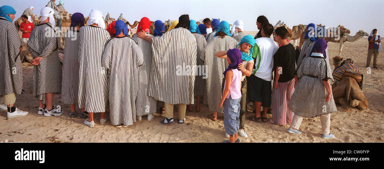Les touristes ne costume Bédouin en préparation pour l'équitation de chameau, Douz, Tunisie. Banque D'Images