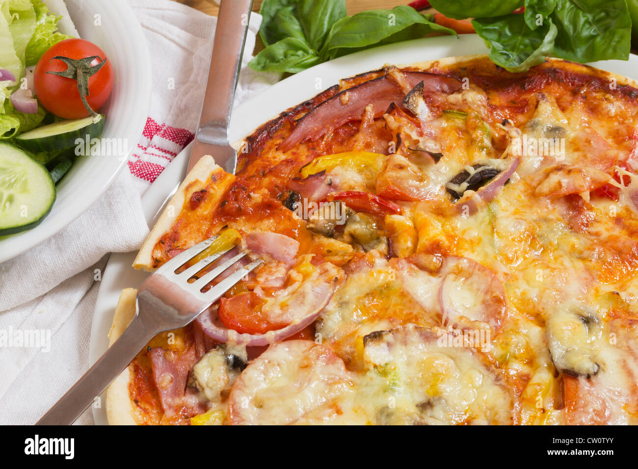 Avec des pizzas jambon, les légumes, le basilic et salade fraîche, toujours la vie comme close-up avec fourchette et couteau pour la cuisine italienne Banque D'Images