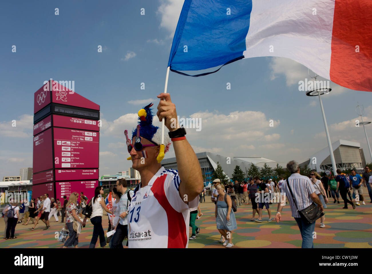 Un fan de sport français détient son drapeau national dans l'air pendant qu'il marche vers un lieu dans le Parc olympique au cours de l'Jeux olympiques de 2012 à Londres. Avec les Hollandais et de nombreux pays baltes, les Français ont fait leur chemin à travers le Channel (La Manche) en grand nombre pour voir leurs héros sportifs effectuer dans les divers endroits de Londres. Banque D'Images