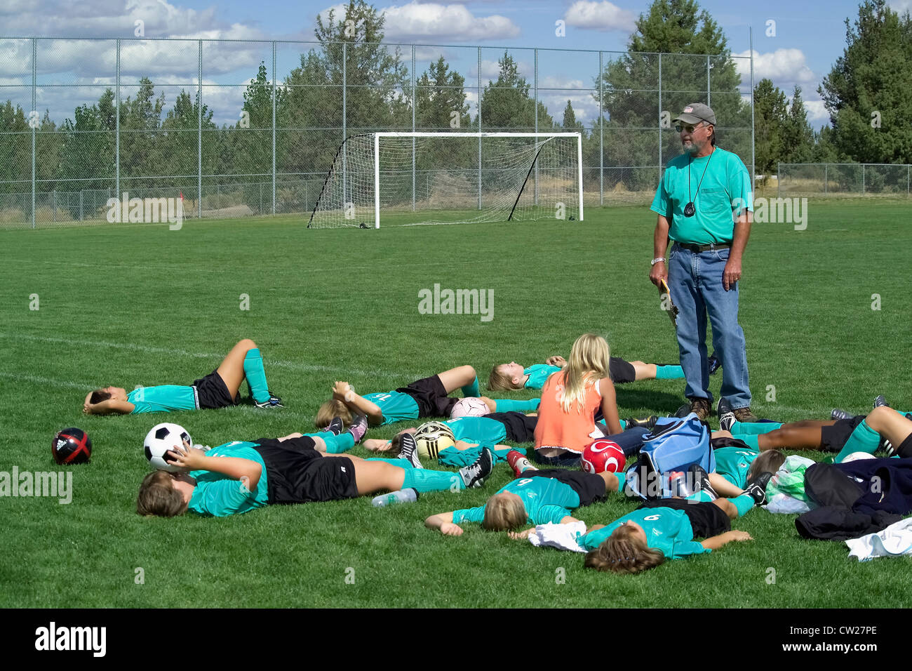 L'entraîneur de soccer masculin donne un entrain parler tandis qu'un jeune de l'équipe des filles repose sur le terrain entre les matches de football après l'école dans la région de Bend, Oregon, USA. Banque D'Images