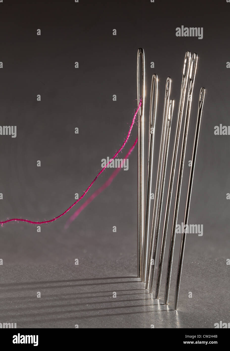 Ligne de couture aiguilles avec fil rouge et d'ombres projetées sur l'arrière-plan Banque D'Images