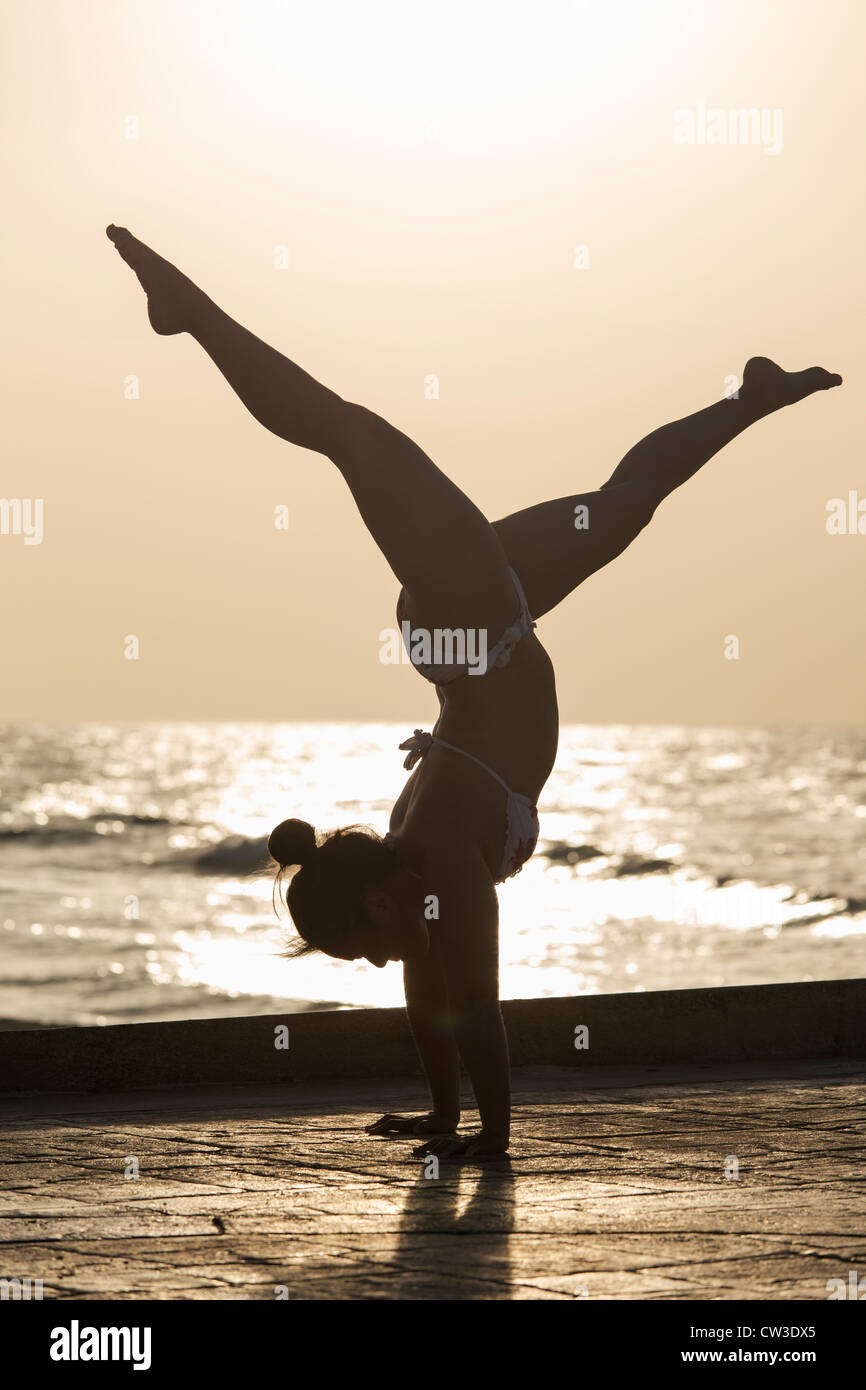 Femme pratiquant un yoga pose au lever du soleil sur une plage Banque D'Images