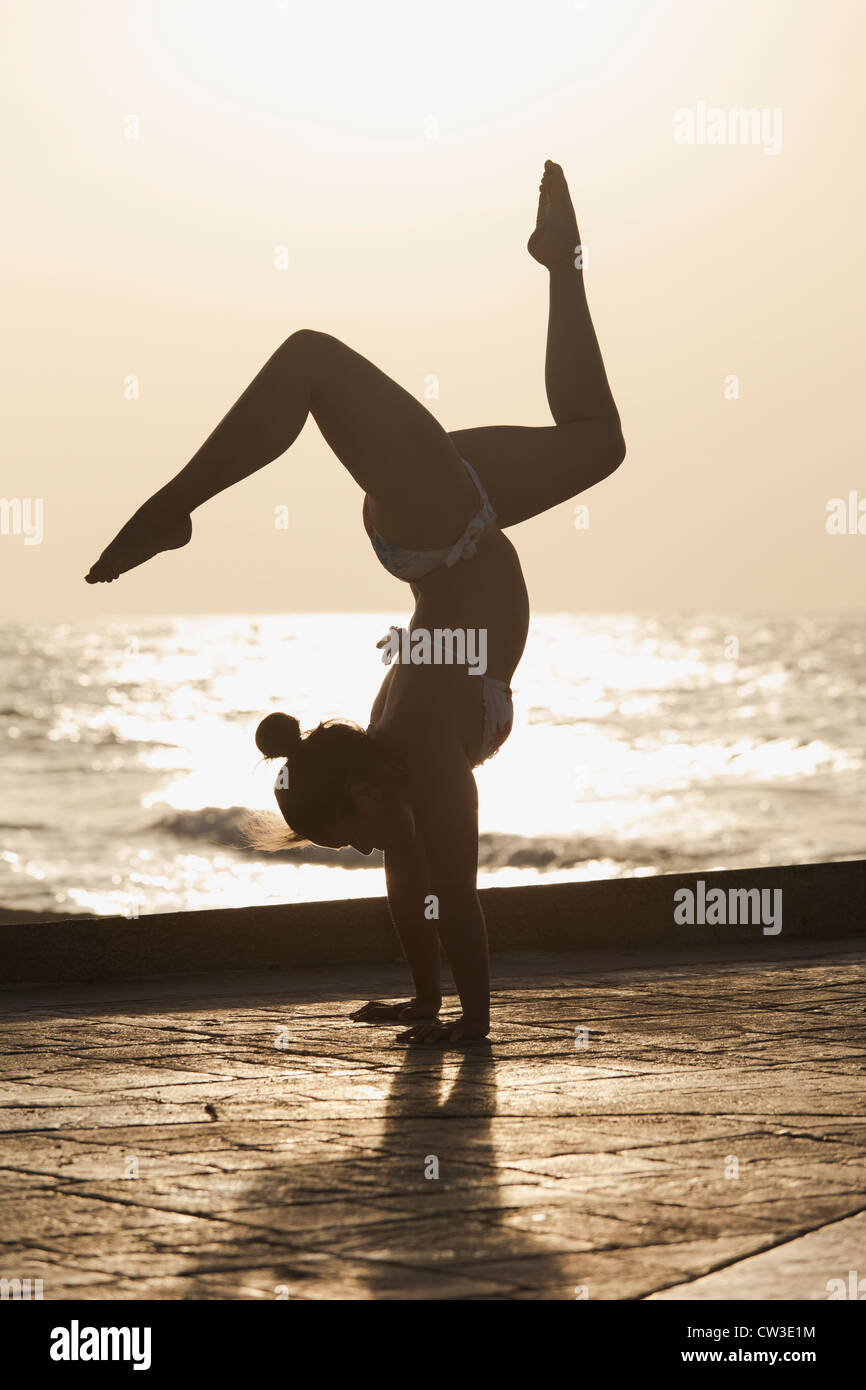 Femme pratiquant un yoga pose au lever du soleil sur une plage Banque D'Images
