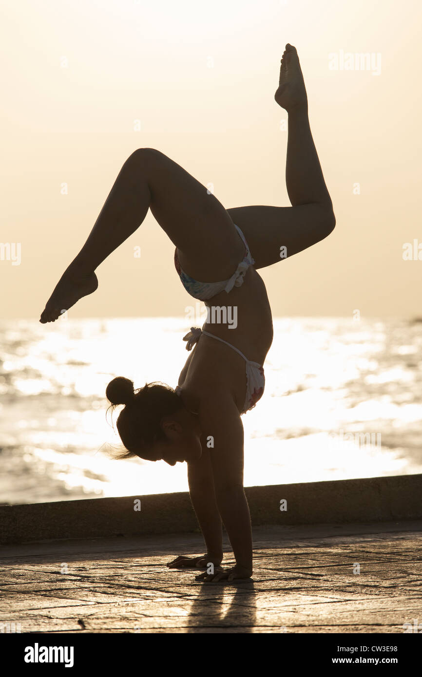 Femme pratiquant un yoga pose au lever du soleil sur une plage Banque D'Images