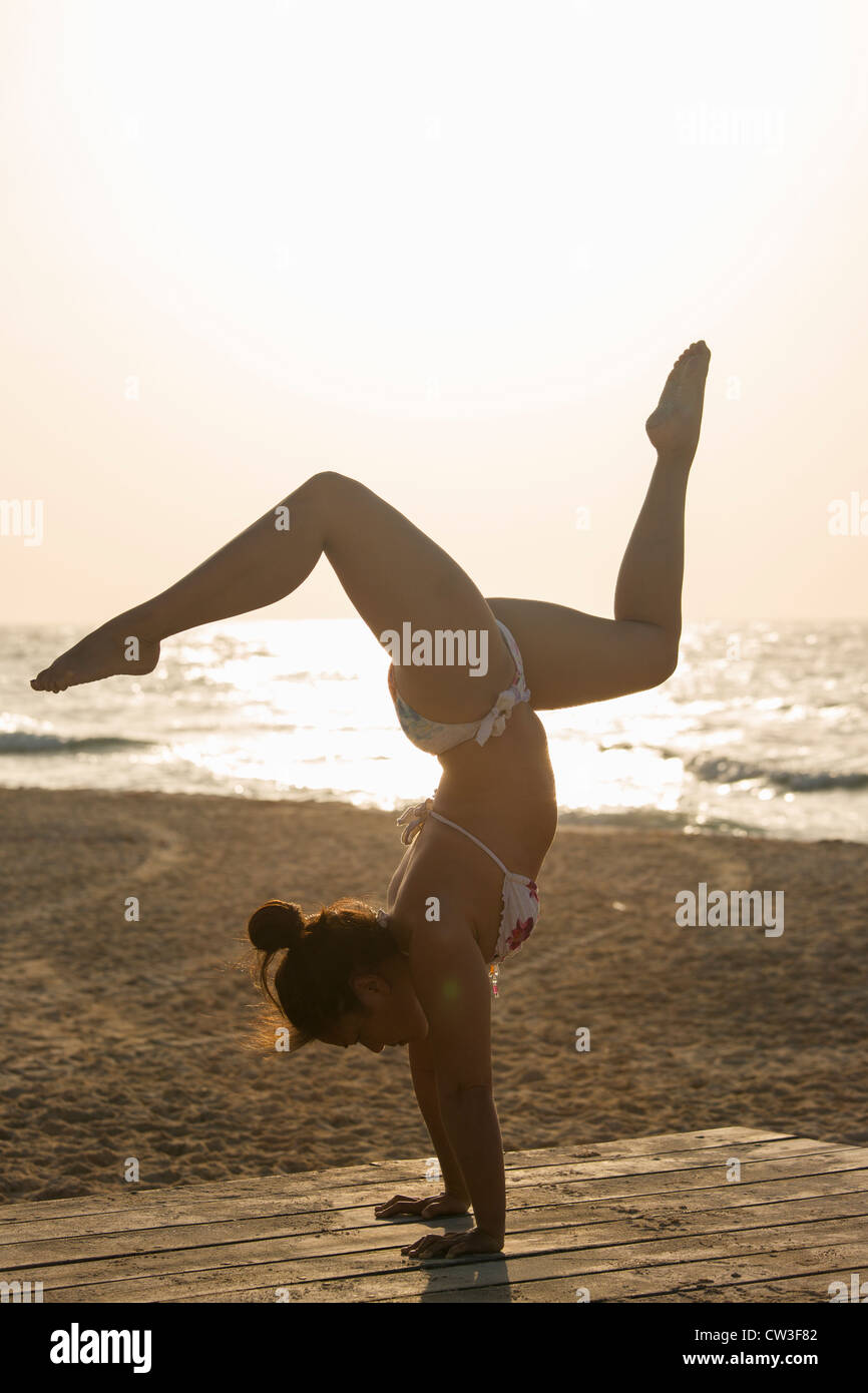 Femme pratiquant un yoga pose au lever du soleil sur une plage Banque D'Images