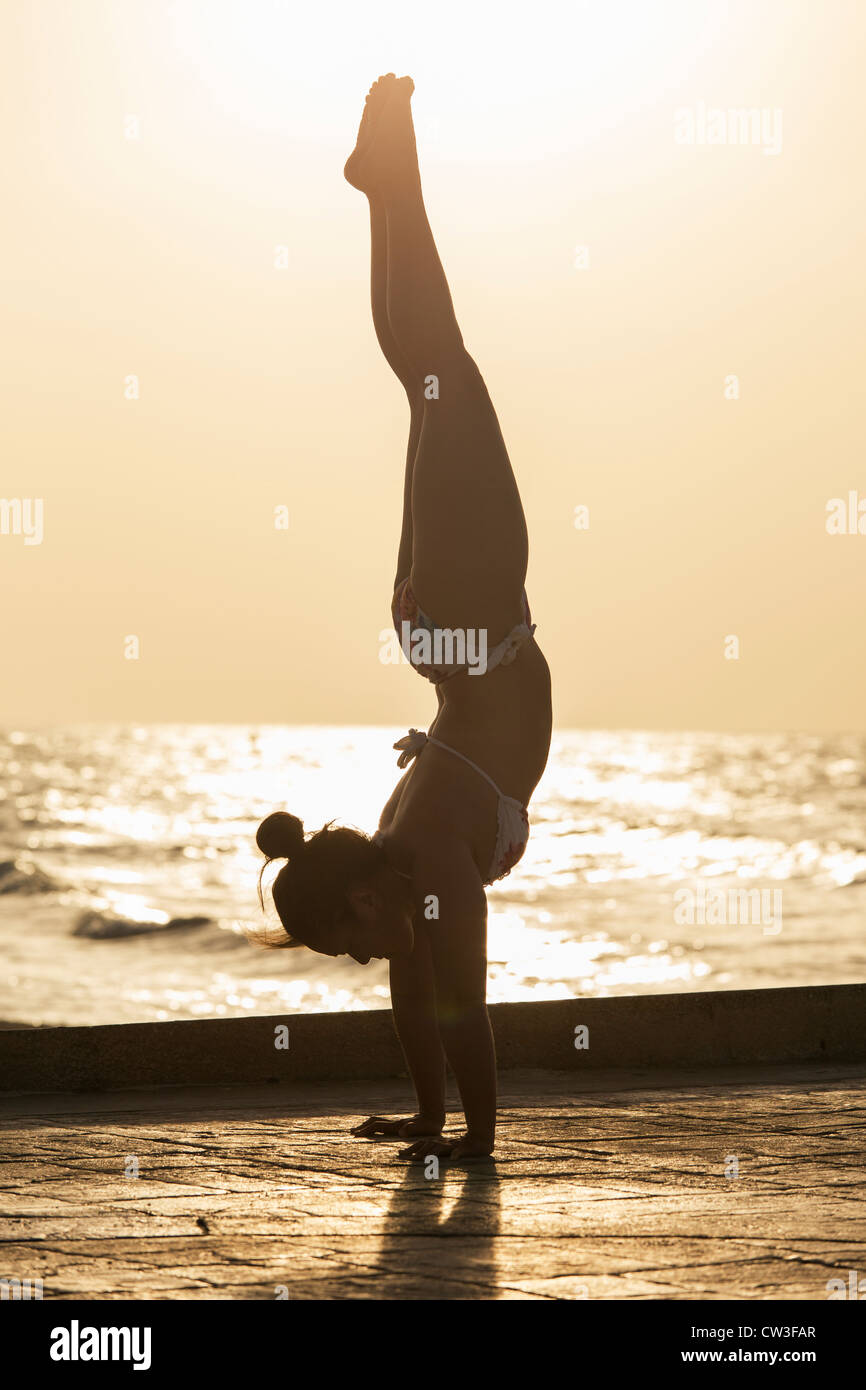Femme pratiquant un yoga pose au lever du soleil sur une plage Banque D'Images