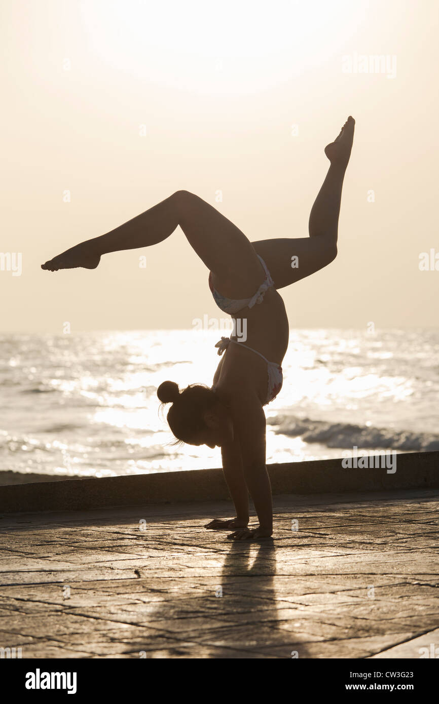 Femme pratiquant un yoga pose au lever du soleil sur une plage Banque D'Images