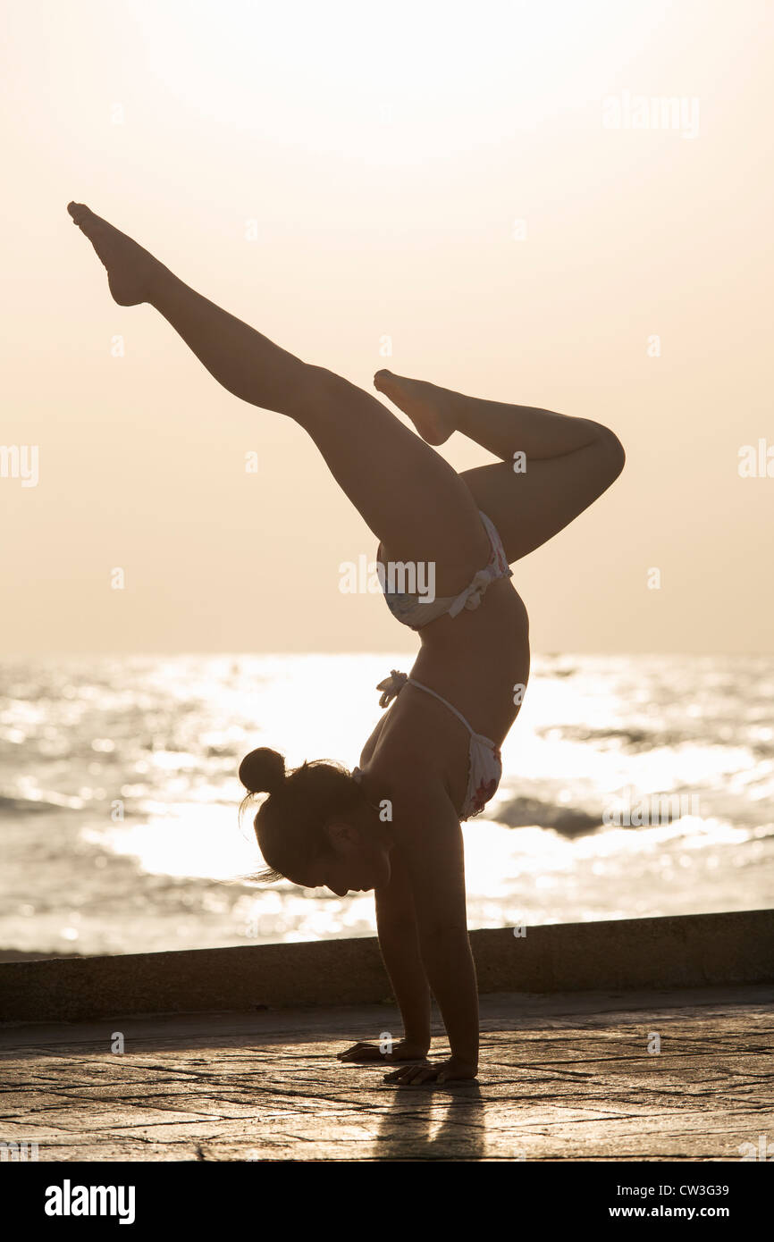 Femme pratiquant un yoga pose au lever du soleil sur une plage Banque D'Images