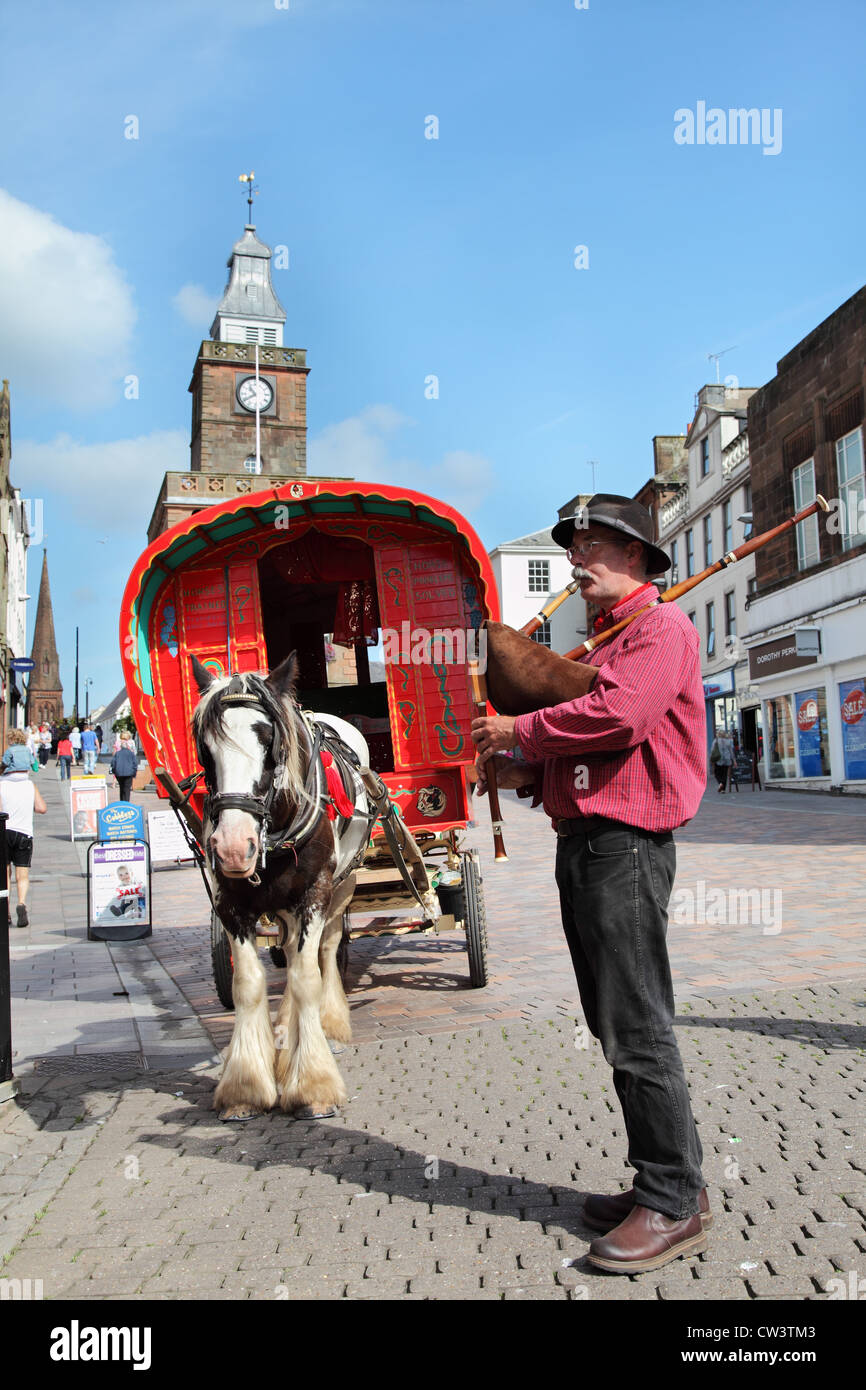 Tuyaux homme jouant en face de style Gypsy Caravan à chevaux à Dumfries, Écosse, Royaume-Uni Banque D'Images