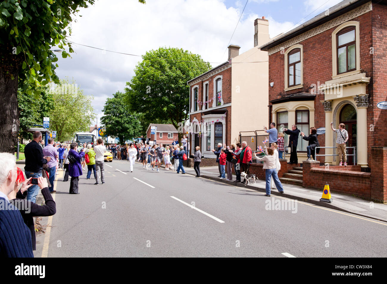 Un porteur de flambeau olympique fonctionne en bas nouvelle route, Willenhall, Midlands de l'Ouest dans le cadre du relais de la flamme des Jeux Olympiques de Londres 2012. Banque D'Images