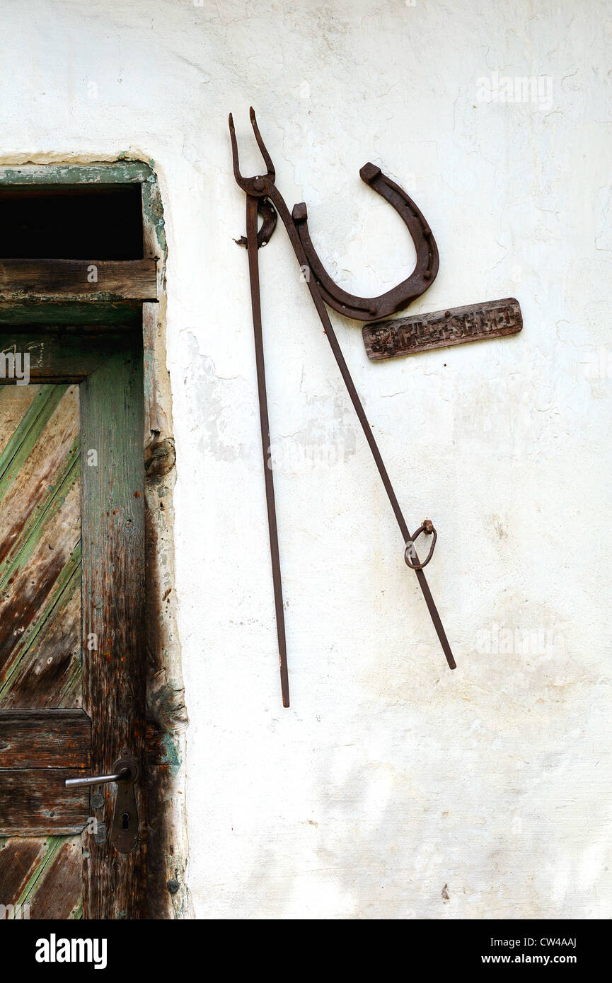 Horse Shoe et forgerons languettes de métal monté sur un mur de la ferme blanche à côté d'une porte en bois lambrissé. Banque D'Images