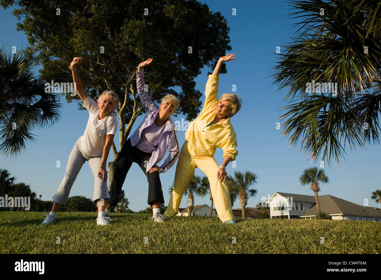 Cheerful senior woman exercising on grass avec main sur genou et bras levés Banque D'Images