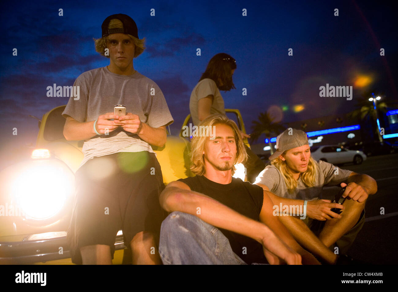 Des amis à l'aide de téléphones mobiles par une voiture à l'aire de stationnement Banque D'Images