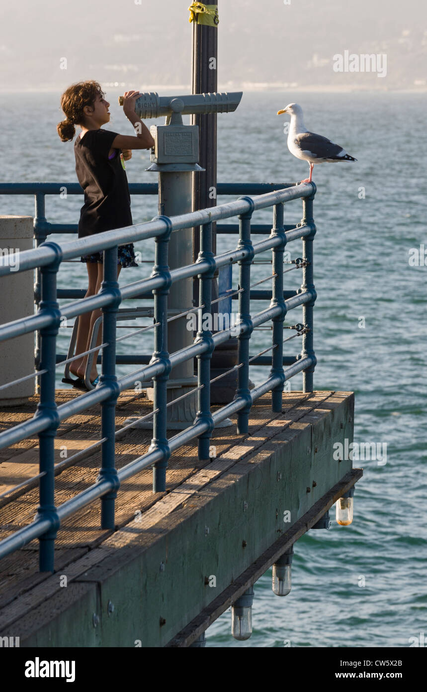 Fille de regarder à travers un télescope, la jetée de Santa Monica, Santa Monica, Californie. Banque D'Images