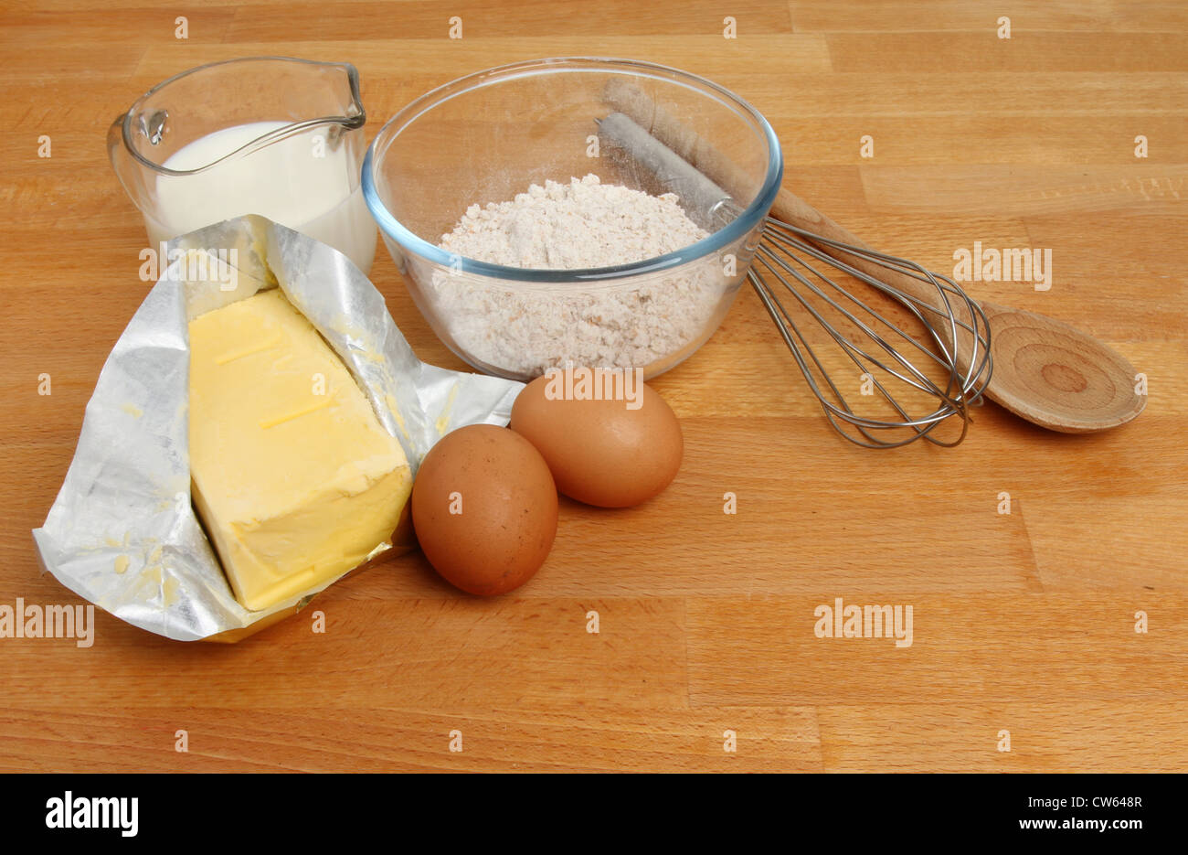 Ingrédients, la farine, les œufs, la margarine, le lait et des ustensiles de cuisine sur un plan de travail en bois Banque D'Images