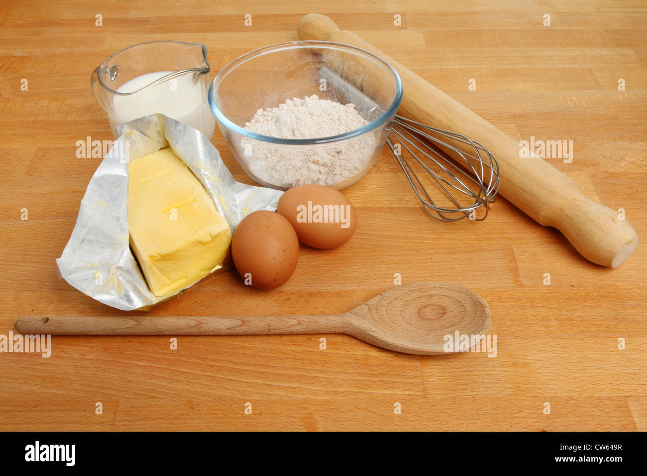 Ingrédients de cuisson, farine, œufs, lait et la margarine à l'aide d'un fouet, cuillère en bois et un rouleau à pâtisserie sur un plan de travail en bois Banque D'Images