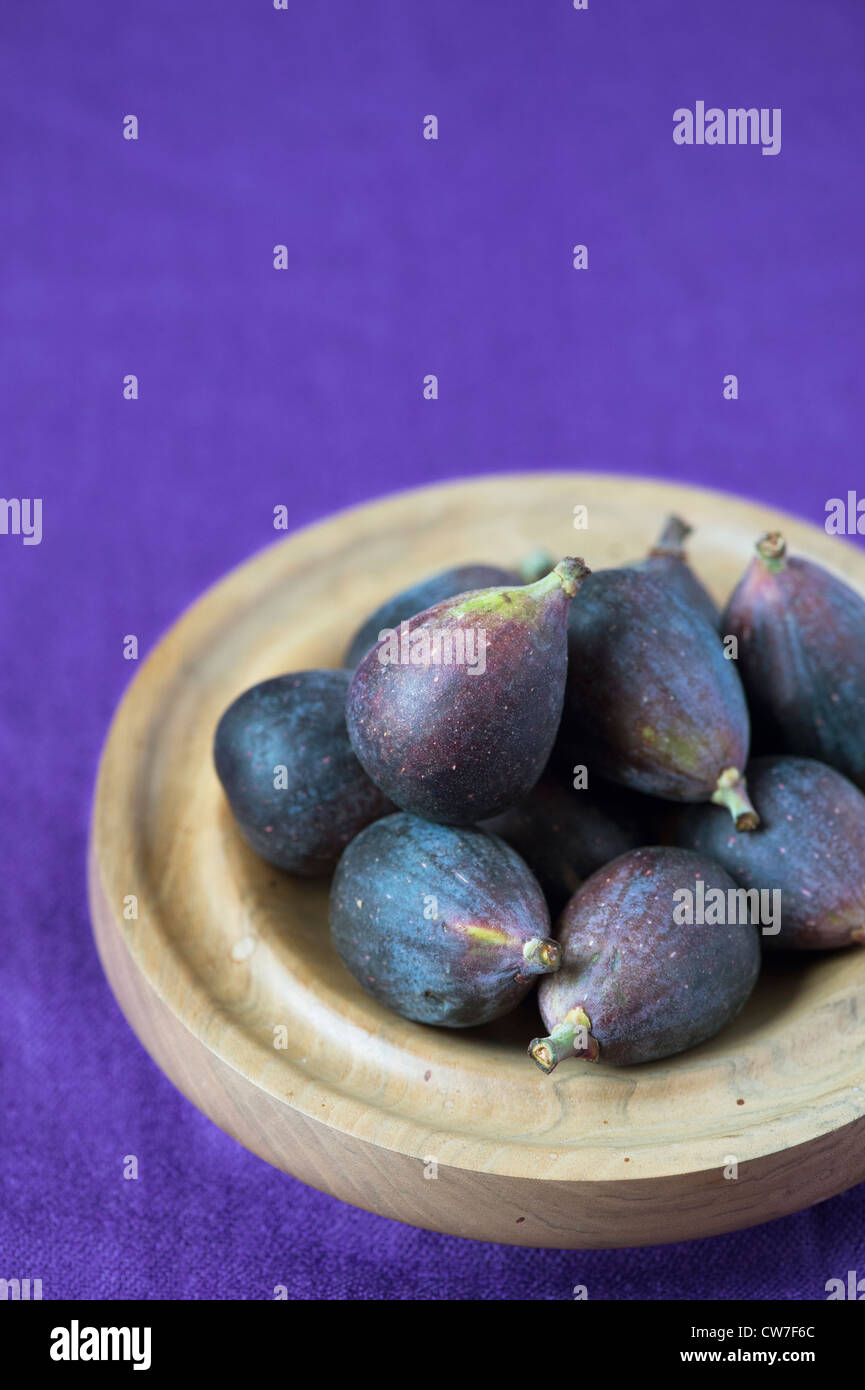 Ficus carica . Figues fraîches entières dans un bol en bois sur fond violet Banque D'Images