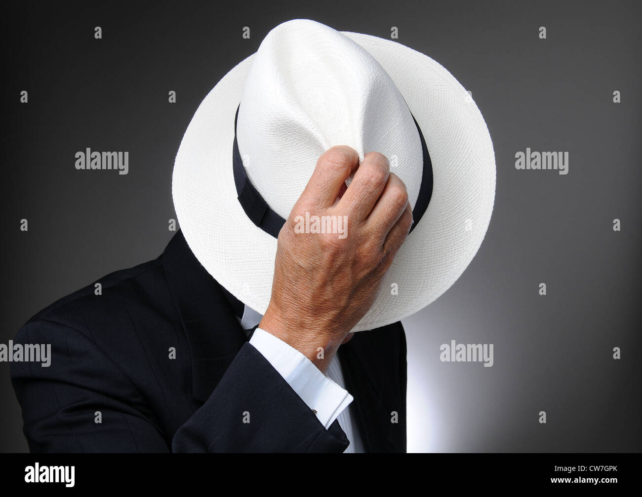 L'homme en smoking se cacher derrière son chapeau. Gros plan horizontal sur un fond gris. Banque D'Images