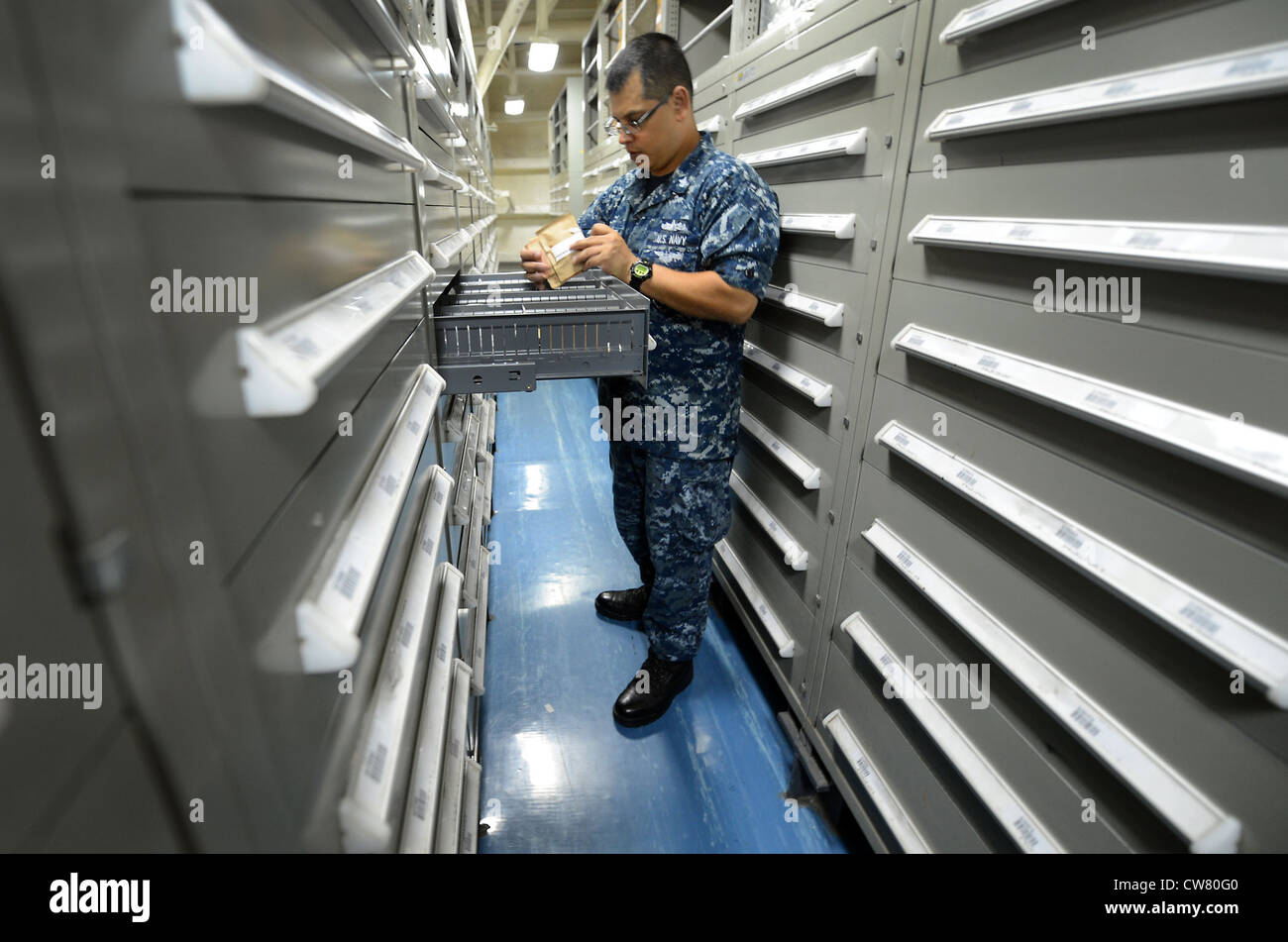 Spécialiste logistique 1ère classe (SW/AW) Adam Martinez recherche des pièces dans les tiroirs d'approvisionnement situés dans le département d'approvisionnement à bord du navire d'assaut amphibie USS Bonhomme Richard (LHD 6). Bonhomme Richard, commandé par le capitaine Dusek, est le navire principal du seul groupe amphibie prêt à être déployé à l'avant. Banque D'Images