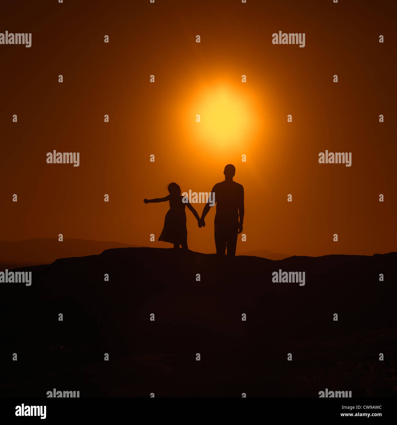Père et fille debout main dans la main au coucher du soleil sur une colline Banque D'Images