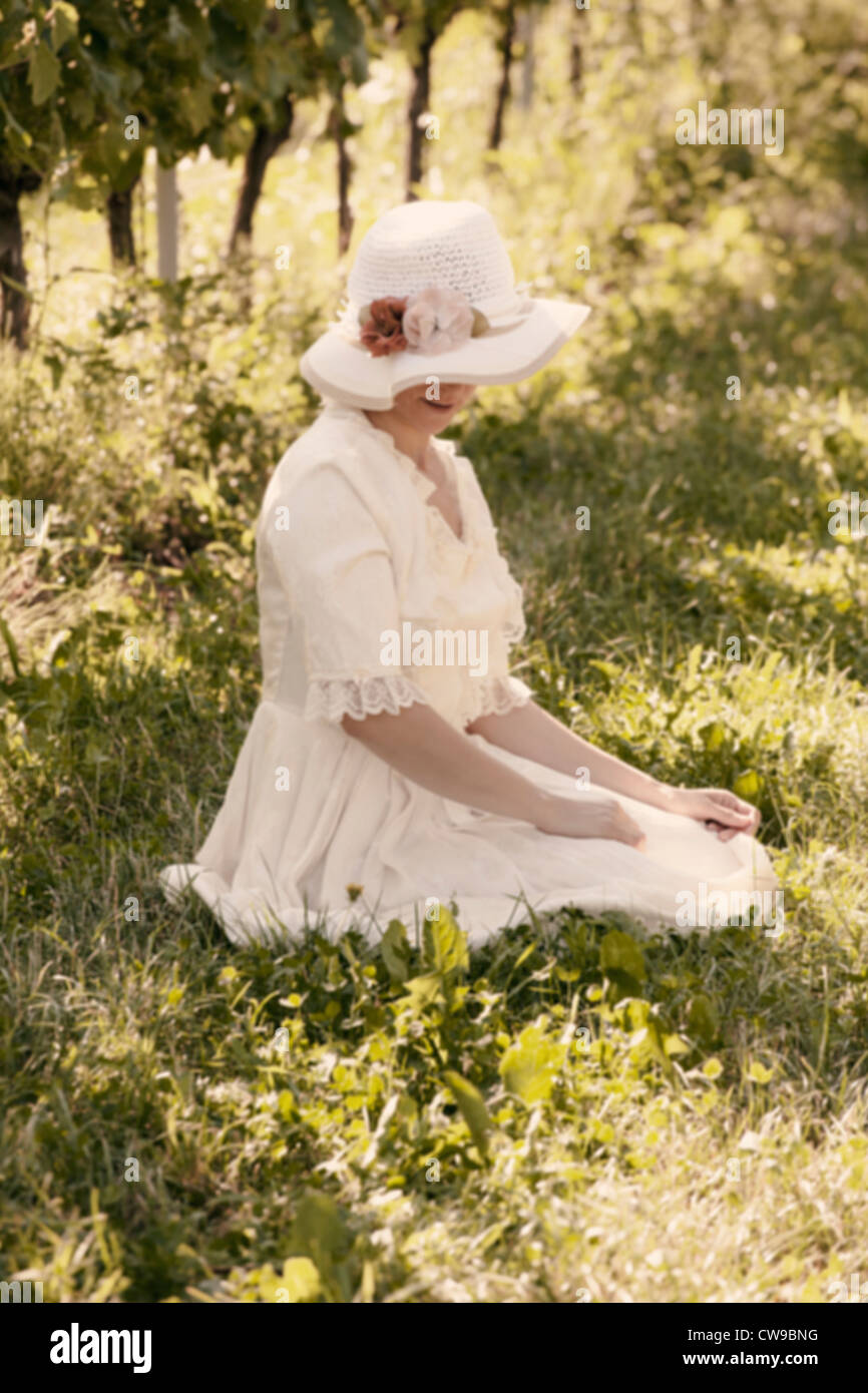 Une femme dans une robe victorienne blanche assise sur l'herbe entre les vignes Banque D'Images