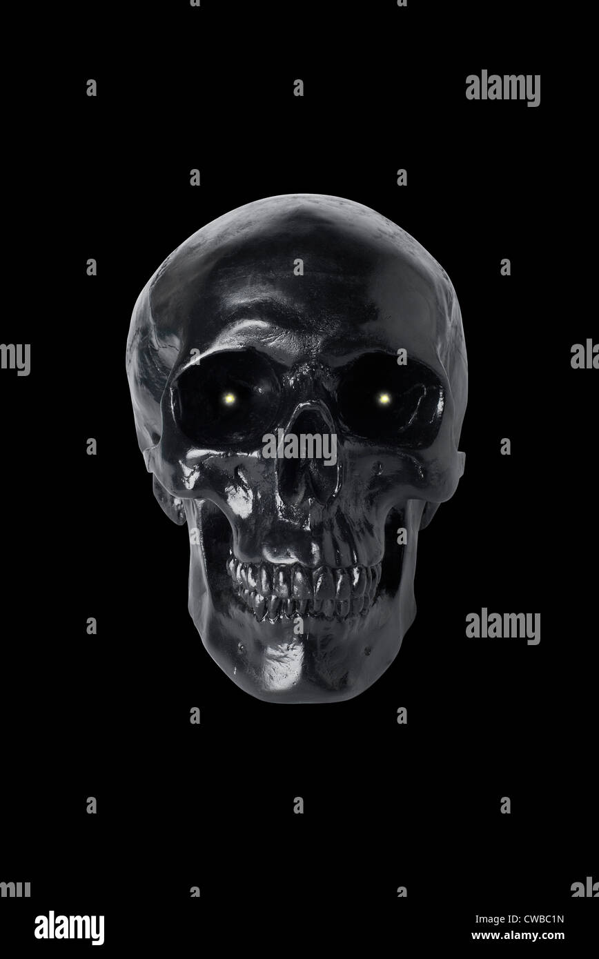 Crâne noir avec des yeux rougeoyants isolé sur fond noir Banque D'Images