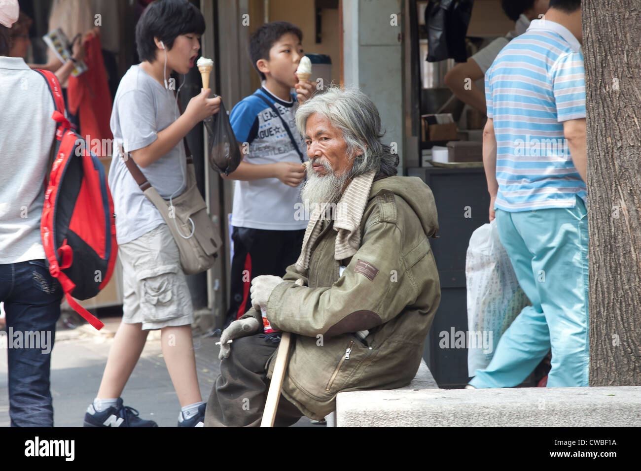 Un sans-abri Le coréen homme portant un lourd manteau se dresse au milieu de tous les gens sur une chaude journée d'été. Banque D'Images