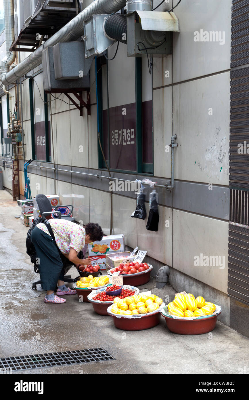 Une femme coréenne vend des fruits et légumes par un bâtiment sur un trottoir près de Séoul, Corée. Banque D'Images
