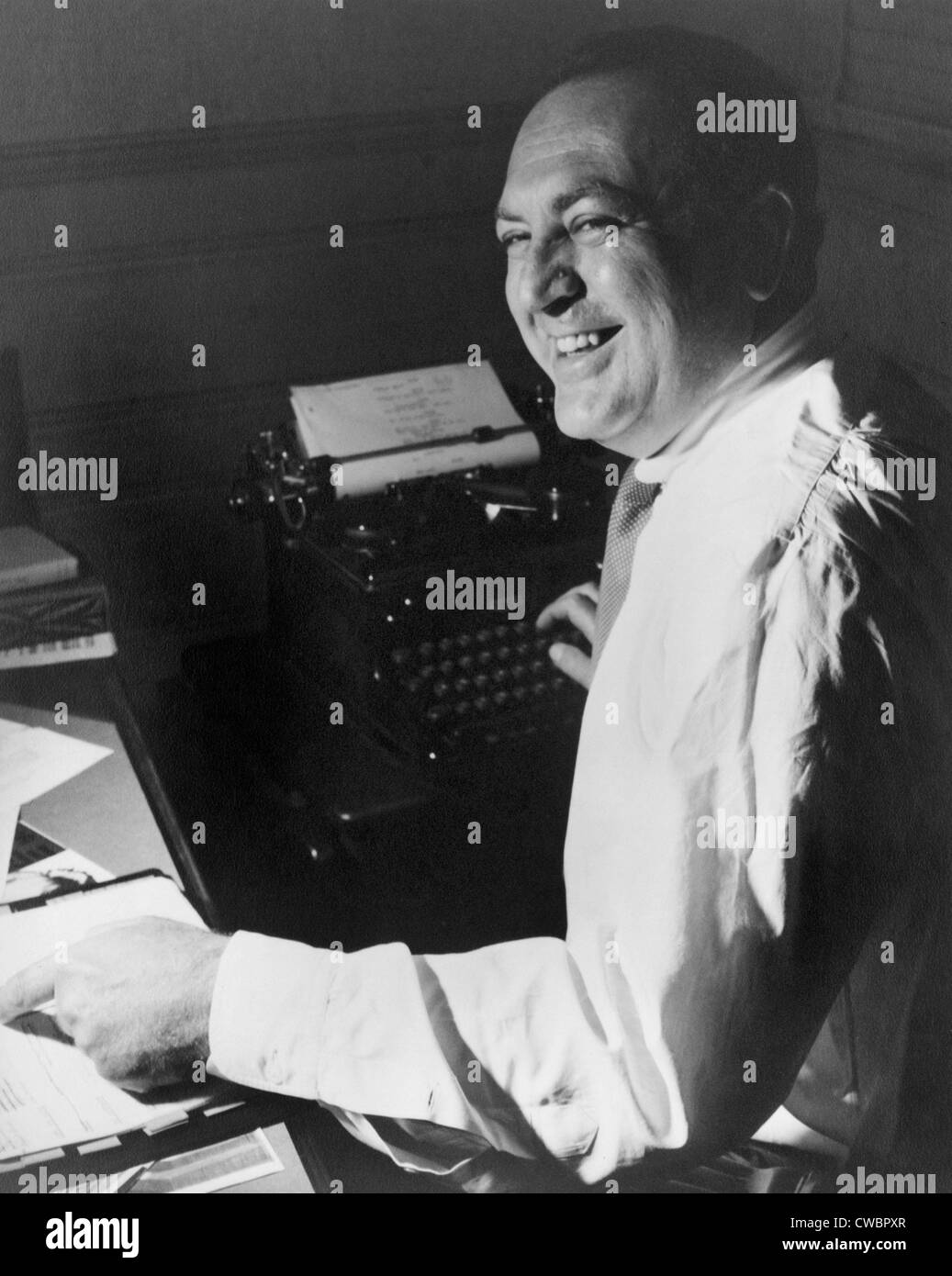 Producteur de films, Val Lewton (1904-1951), travaillant à son bureau, avec une main sur un script et l'autre sur une machine à écrire. Ca. 1945. Banque D'Images