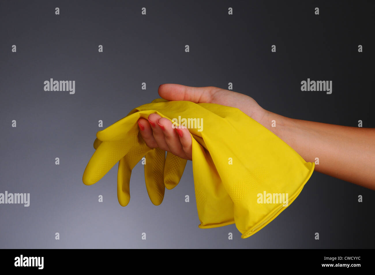 Libre d'une main de femme tenant une paire de gants en caoutchouc jaune sur un fond gris clair à foncé. Banque D'Images
