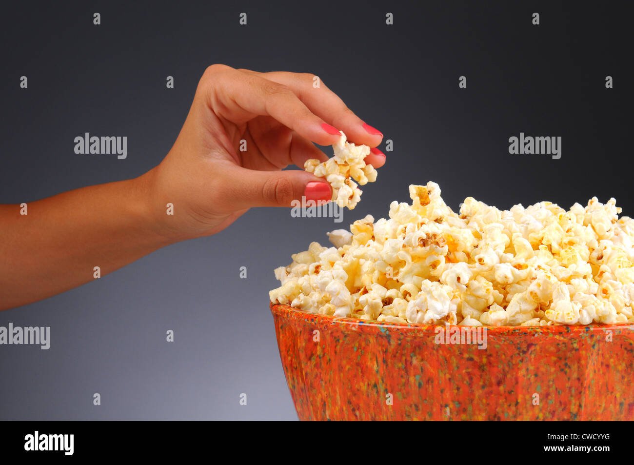 Libre d'une main de femme prendre du popcorn à partir d'un bol. Format horizontal sur une lumière sur fond gris foncé. Banque D'Images