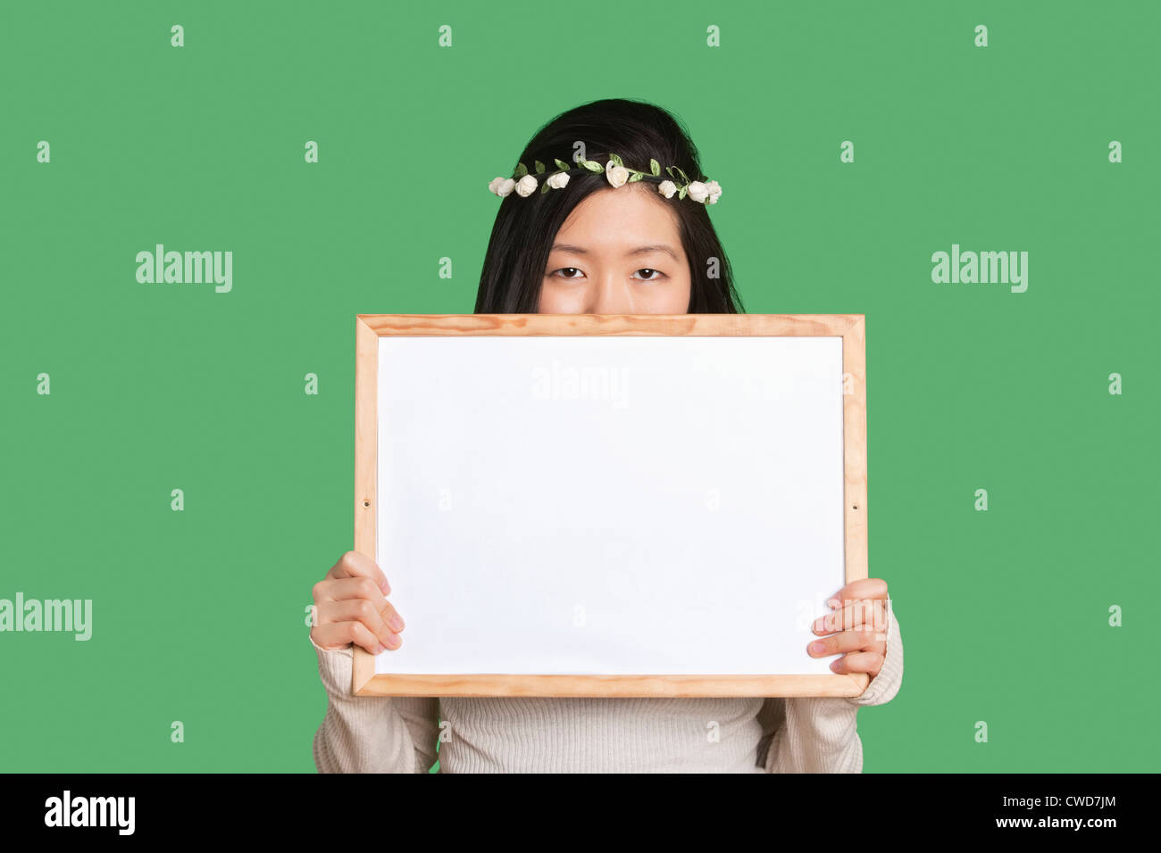 Portrait d'une jeune femme cachant son visage avec un tableau blanc sur fond vert Banque D'Images