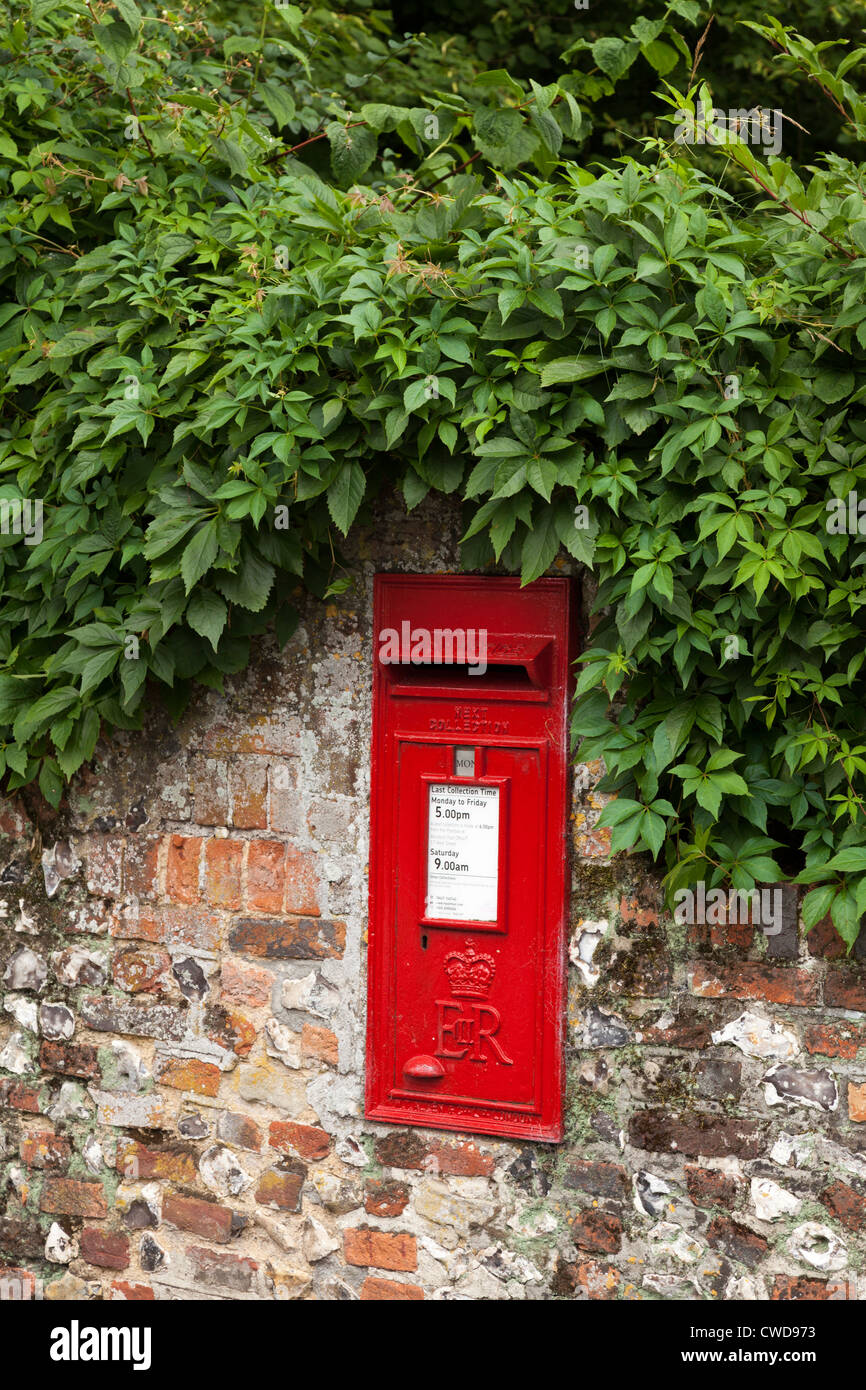 Post box set rouge en silex et brique partiellement couvert par le feuillage Banque D'Images