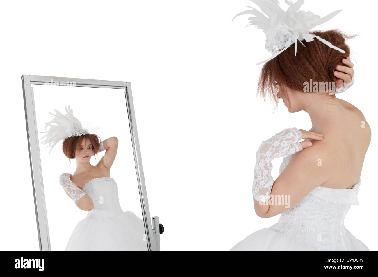 Jeune femme brune en robe de mariée à la recherche d'elle-même en miroir sur fond blanc Banque D'Images