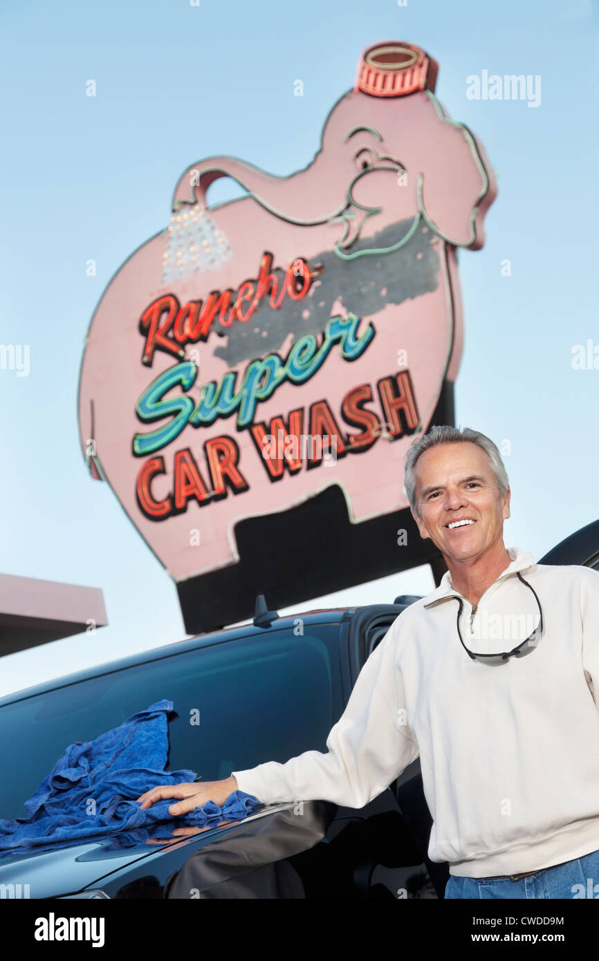 Portrait of mature propriétaire de lavage de voiture l'article ci-dessous pancarte avec véhicule Banque D'Images