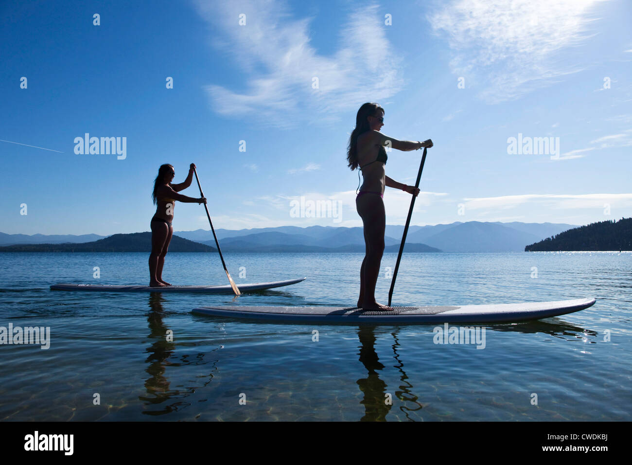 Deux jeunes femmes athlétiques stand up paddle board sur un lac dans la région de Idaho sur une journée ensoleillée. Banque D'Images